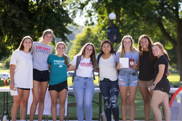 Saint marys students posing together with smiling faces outdoors, with green trees in the background.