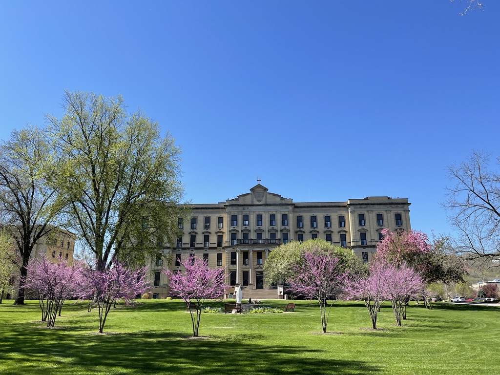 Saint Mary's Campus building in the distance with blooming trees and grass in the foreground.