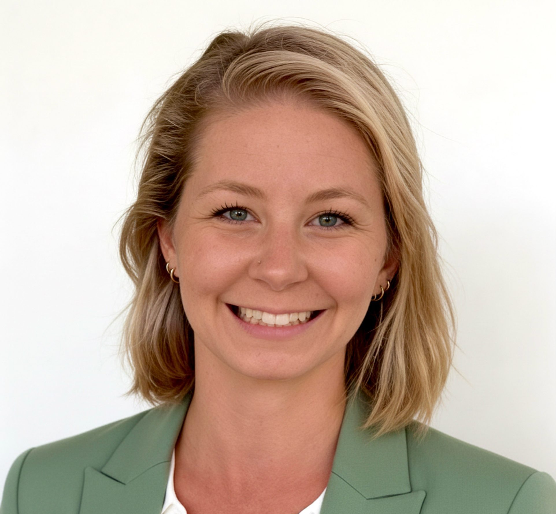 A smiling woman with blonde hair wearing a sage green blazer over a white collared shirt.
